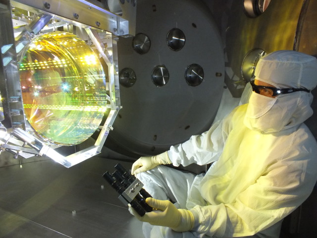 A LIGO optics technician inspects one of LIGO’s core optics by illuminating its surface with light at a glancing angle. (Image Courtesy of LIGO Laboratory)