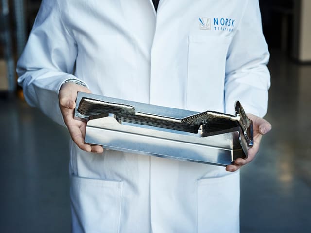 A Norsk Titanium scientist displays a Boeing 787 Dreamliner structural component to demonstrate the near-net-shape RPD buy-to-fly ratio. (Image courtesy of Norsk Titanium.)